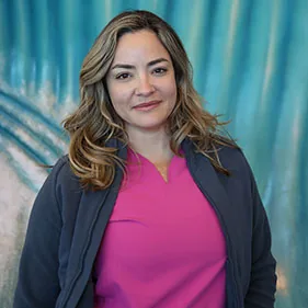 Dr. Yusleimys Torres, general dentist, in a pink top and gray cardigan against a blue backdrop