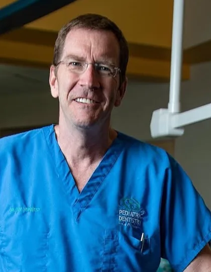 Dr. Tim Verwest in blue scrubs, smiling, standing in the treatment area of Pediatric Dentistry of Florida