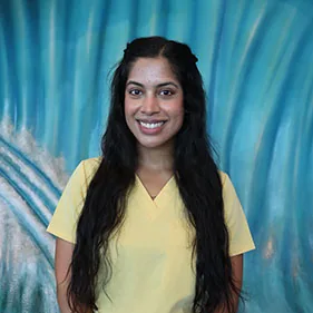 Dr. Riya Walia, pediatric dentist, in a yellow top against a blue backdrop