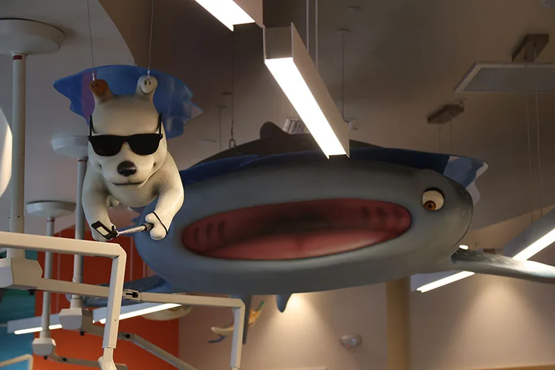 Close-up of Shades, the white dog mascot in black sunglasses, riding the whale shark sculpture in the Naples office